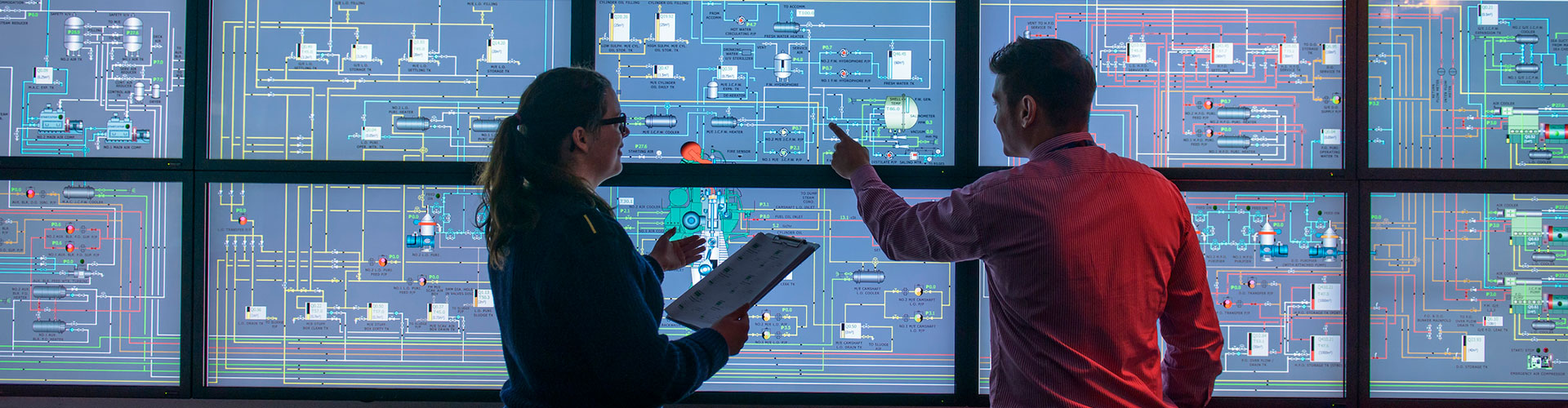 Two people in a control room, looking at a large data screen