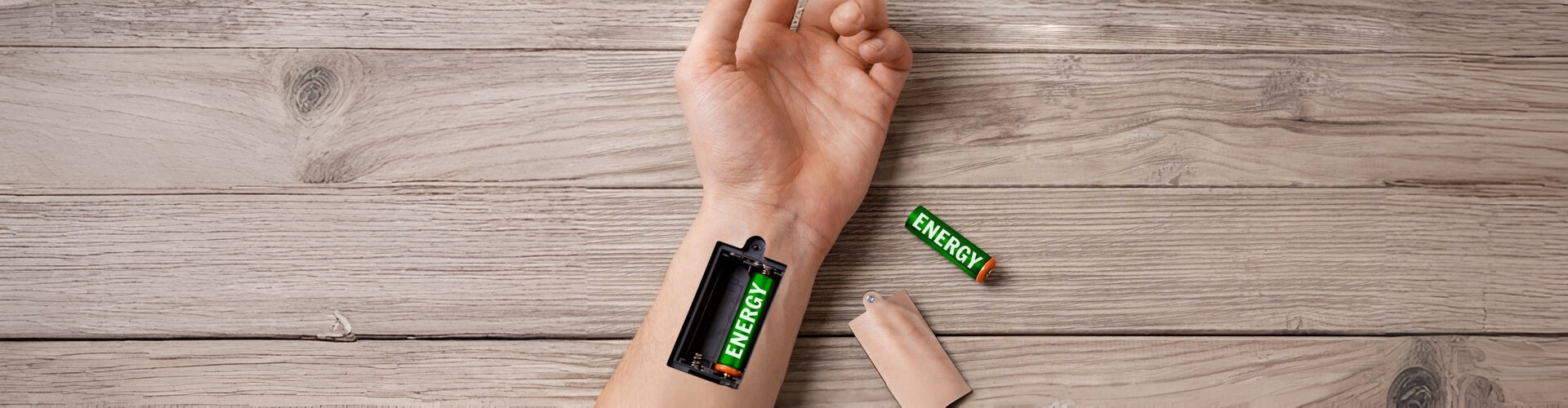 An arm, resting on a wooden table, with a battery port in the wrist, showing one battery installed, and one on the table.