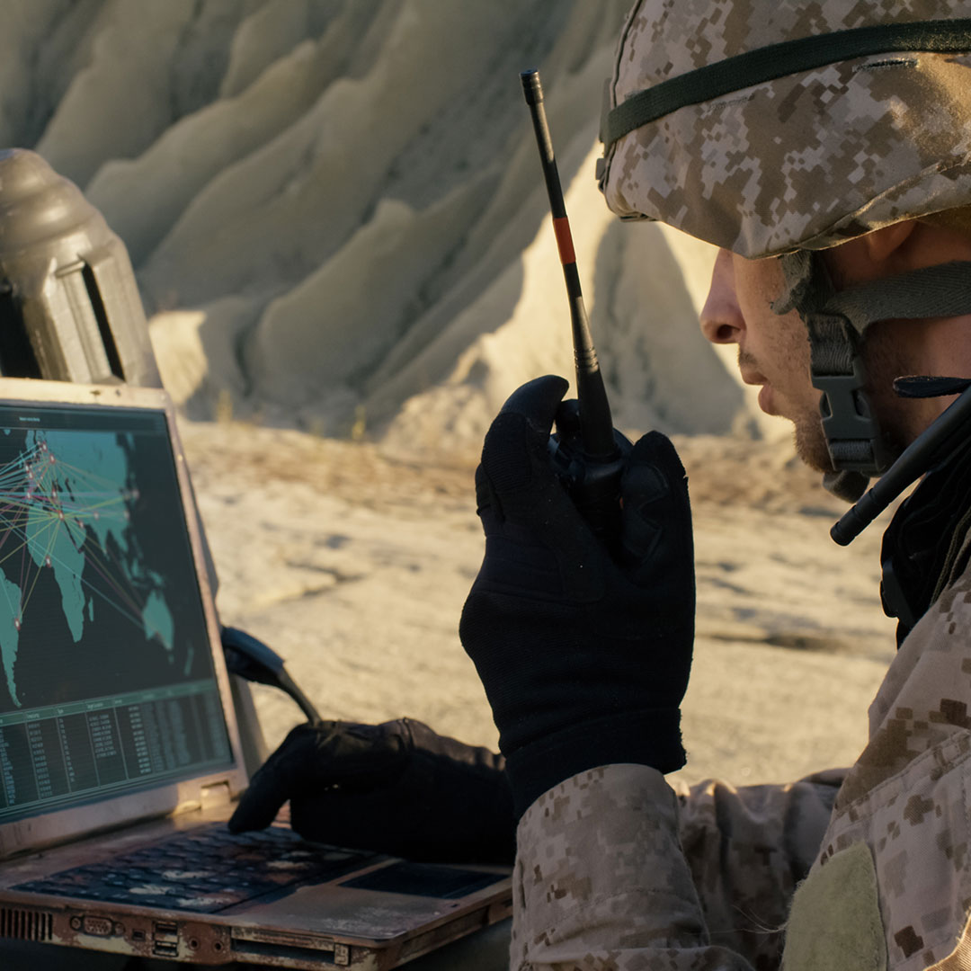 Soldier using laptop and radio for comms during military operation in the desert