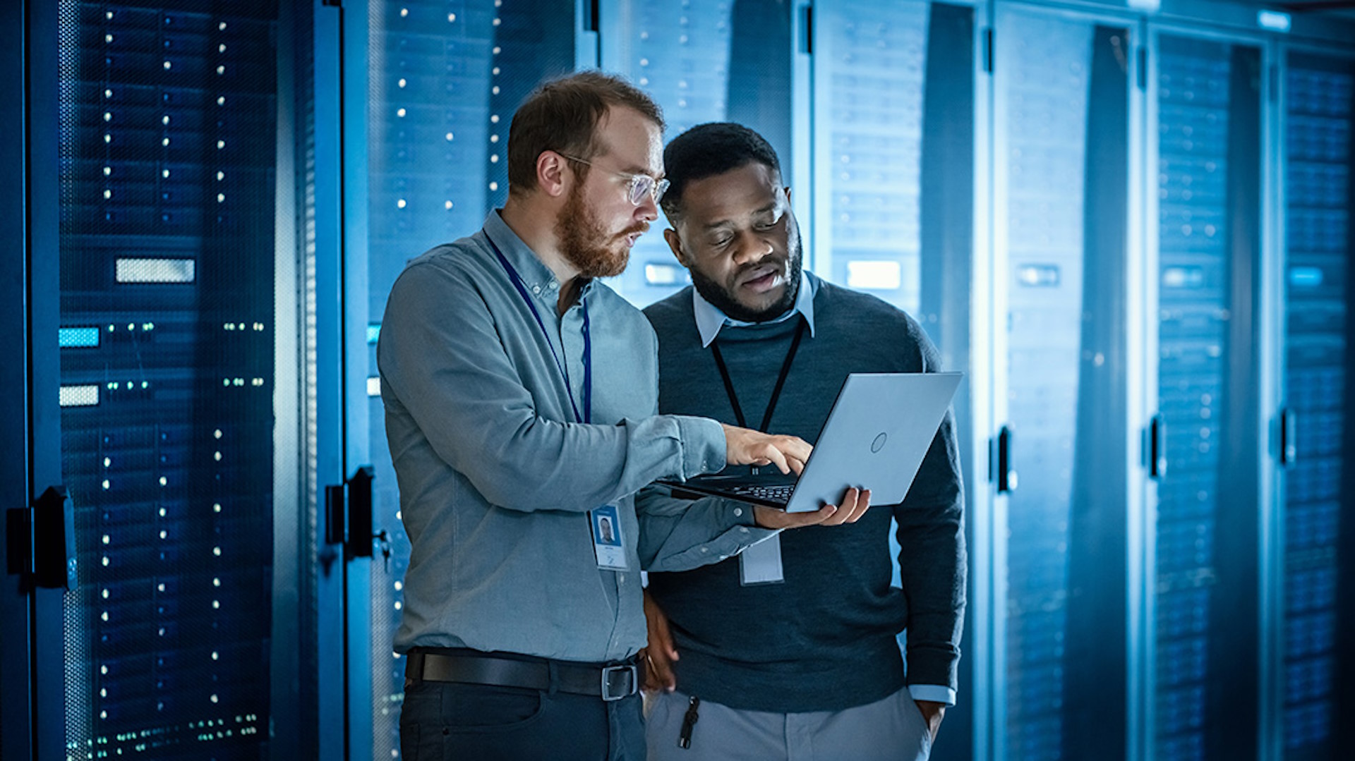 Two people looking at a laptop, in front of servers
